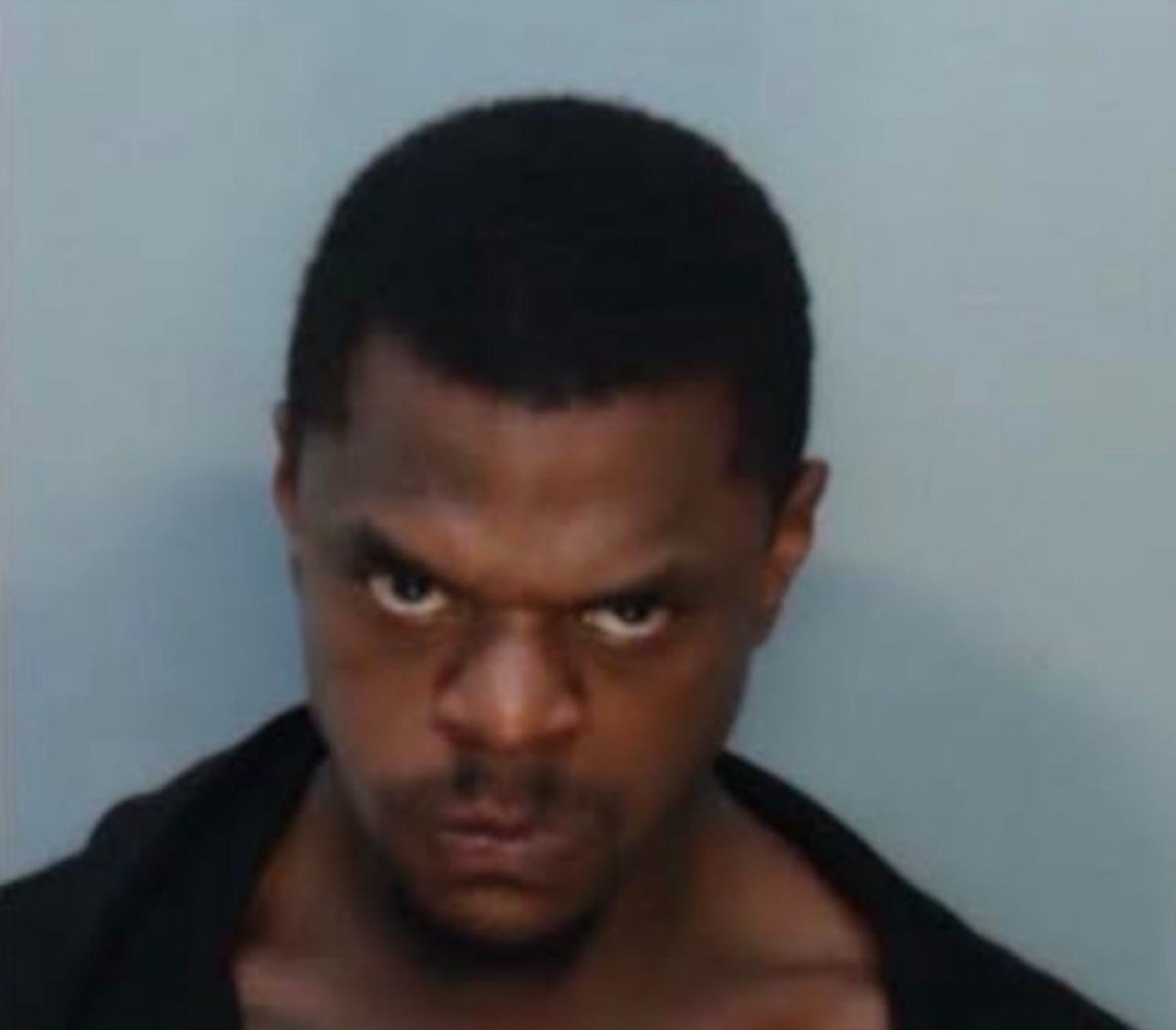 Man in a mugshot-style photo glaring into the camera with deeply furrowed, menacing brows