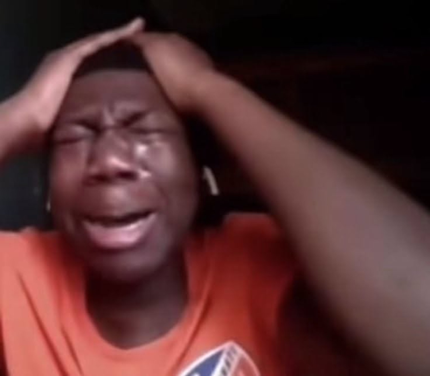 Guy in an orange shirt clutching his head and sobbing in despair