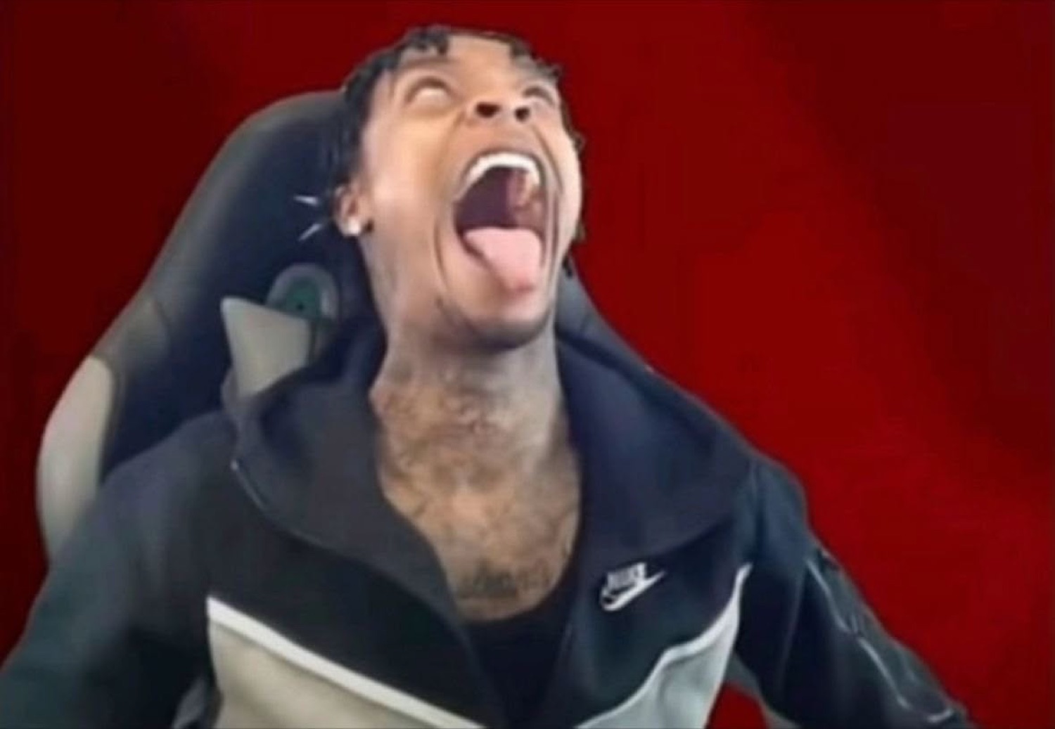 Man in a gaming chair throwing his head back laughing with mouth wide open against a red background