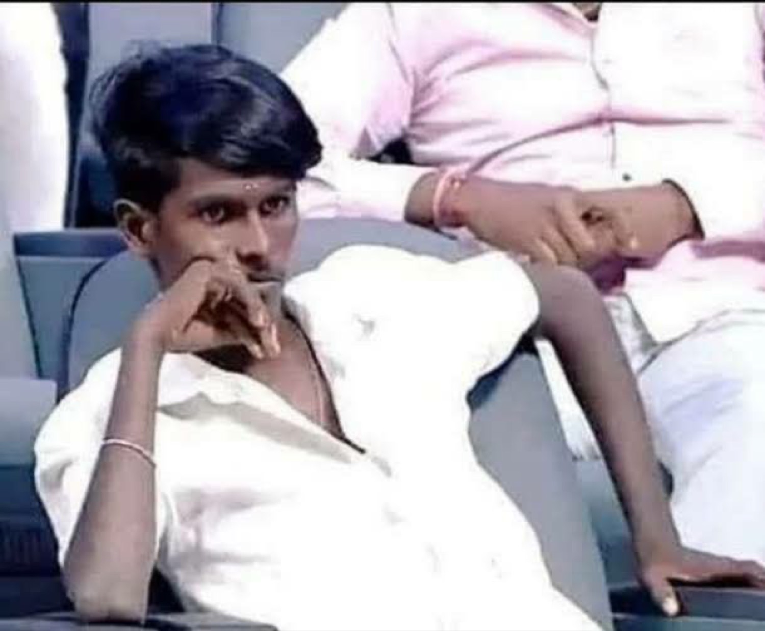 Skinny guy lounging with his hand on his chin looking smug