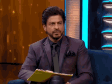 Shah Rukh Khan on a talk show lowering a card and gesturing with a smirk
