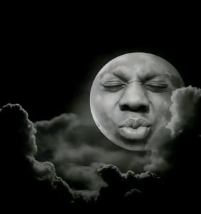 Black-and-white moon with a human face puckering up for a kiss above the clouds