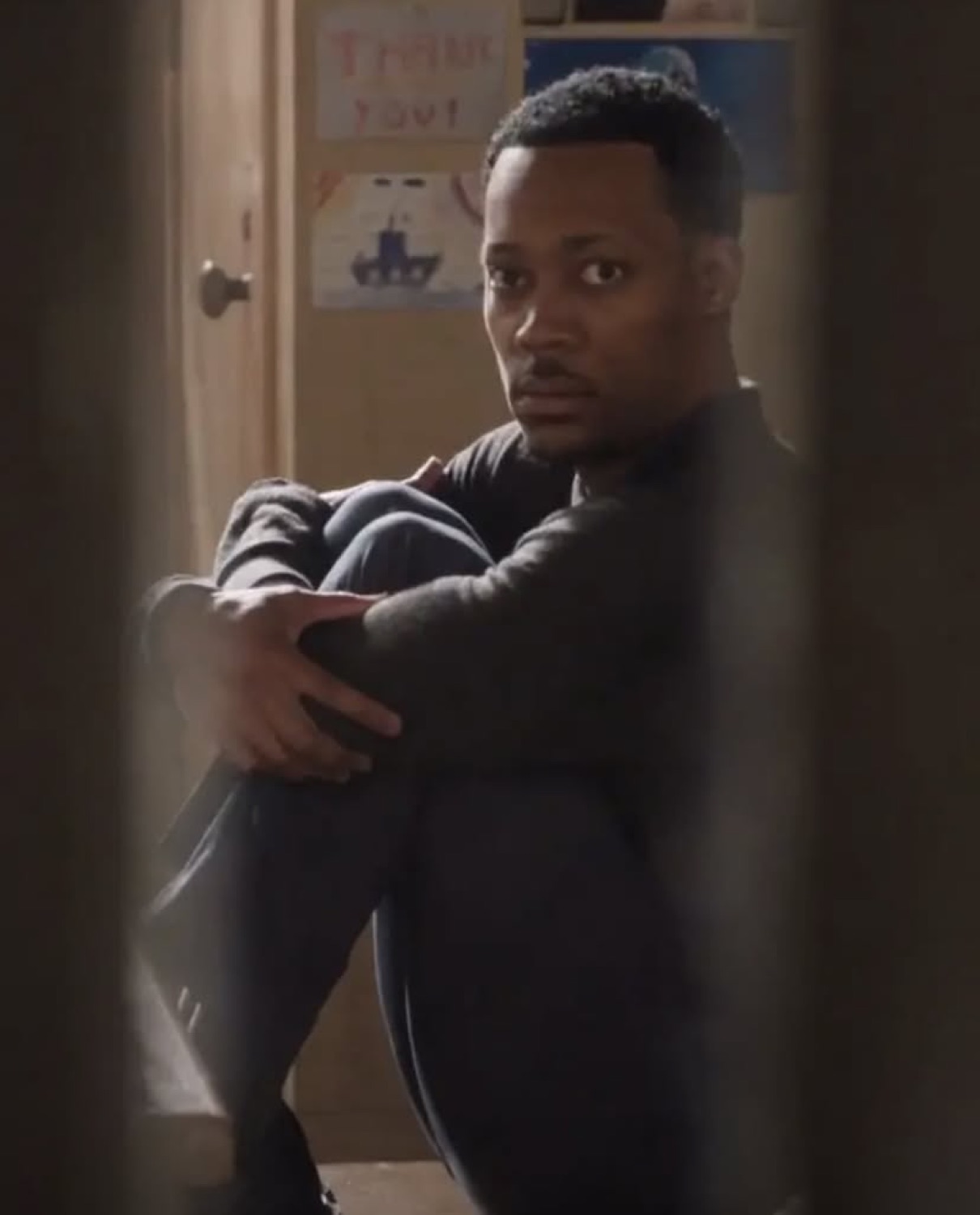Man hugging his knees on the floor and looking over his shoulder with an anxious expression