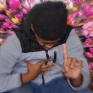 Person surrounded by pink heart balloons giving a peace sign while looking down