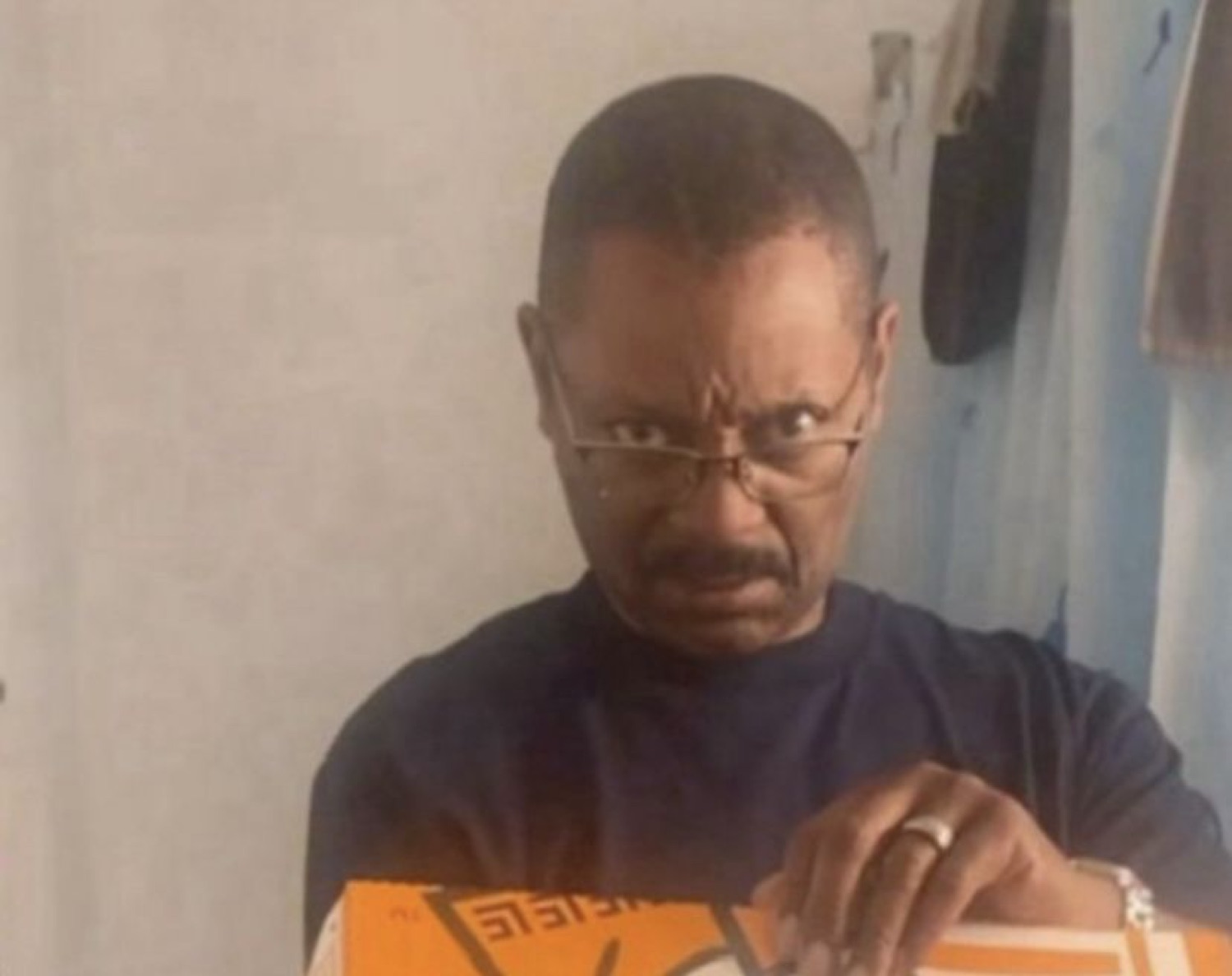 Older man peering over his glasses with a deeply suspicious, stern glare