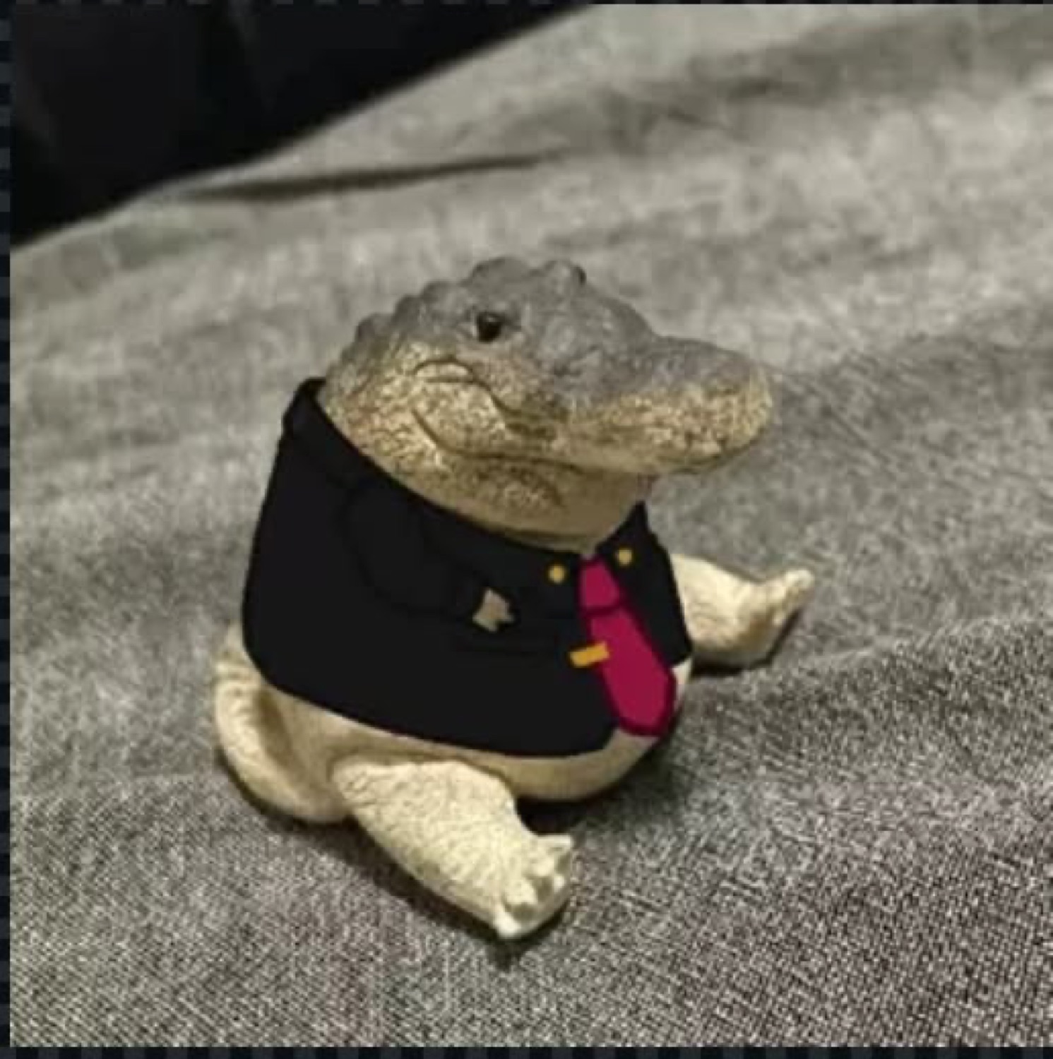 Tiny chubby alligator figurine in a black suit and red tie sitting up like a businessman