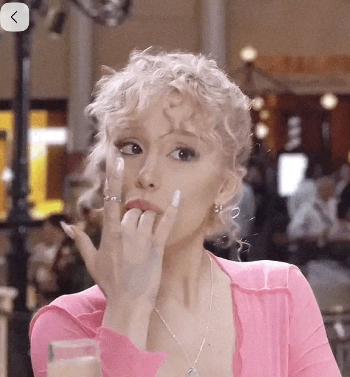Woman in pink glancing sideways while biting her nail nervously
