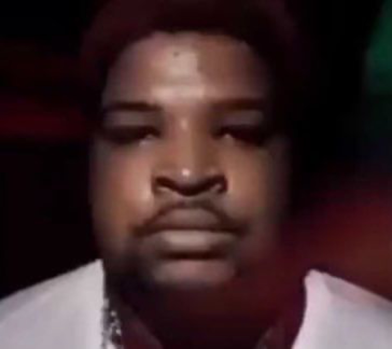 Man staring down with a flat, emotionless deadpan expression in dim light
