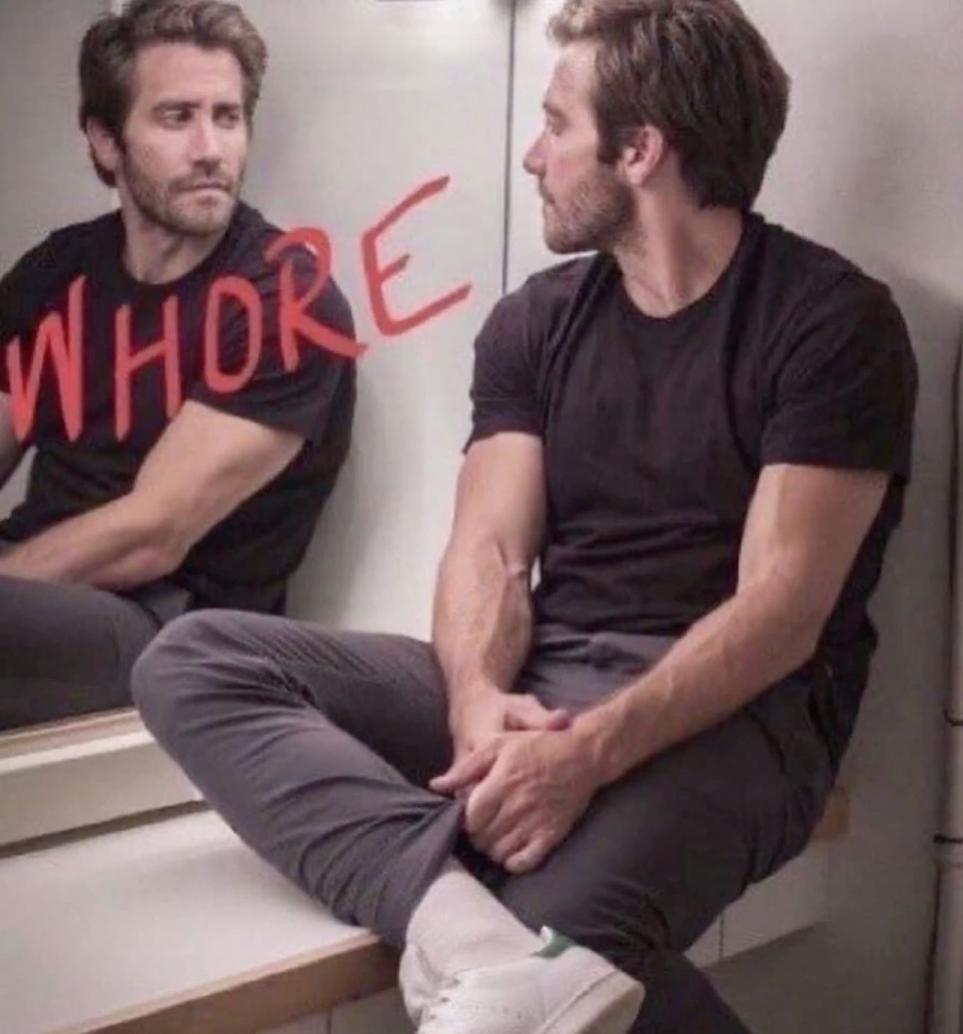 Jake Gyllenhaal sitting calmly by a mirror with 'WHORE' written in red on the glass