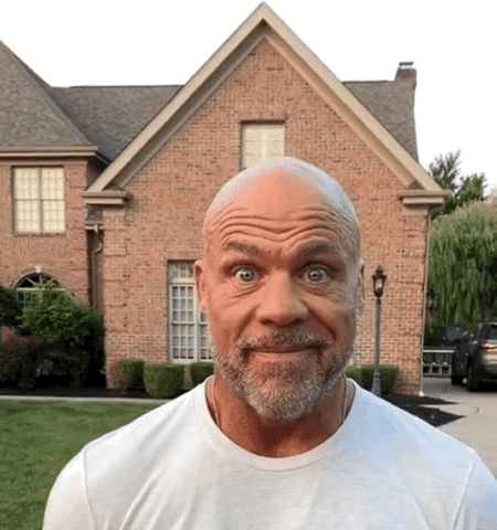 Bald bearded man in front of a brick house with eyebrows raised and eyes wide in shock