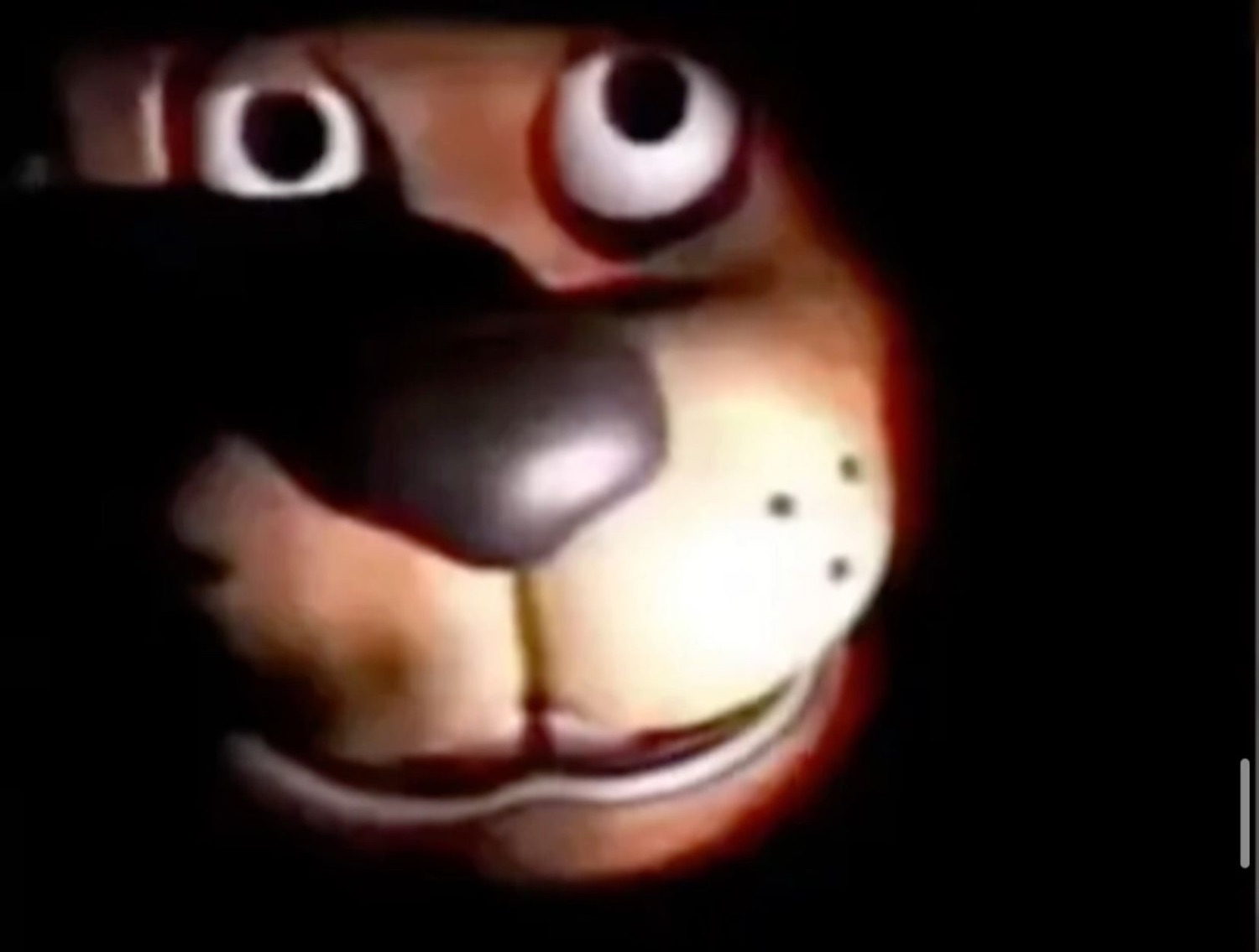 Grainy dark shot of a cartoon dog animatronic face lit up in the shadows