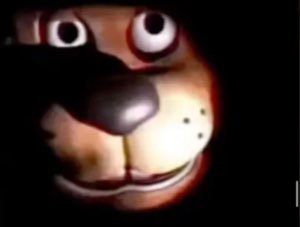 Grainy dark shot of a cartoon dog animatronic face lit up in the shadows
