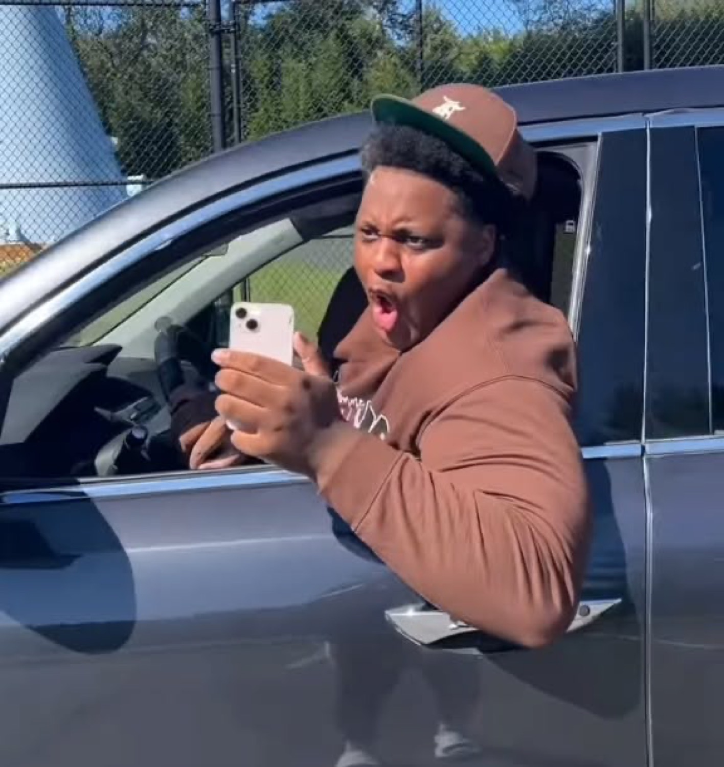 Man leaning out a car window recording his phone with a shocked, disgusted grimace