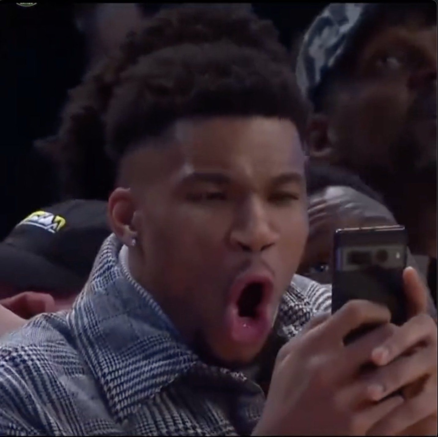 Young man at a basketball game staring at his phone with mouth wide open in disbelief