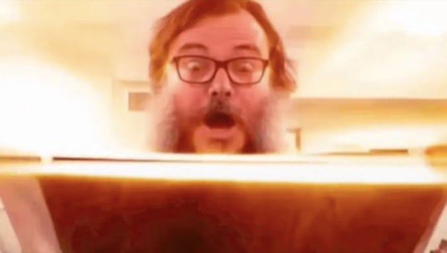 Bearded guy in glasses gasping at a glowing box like it just changed his life