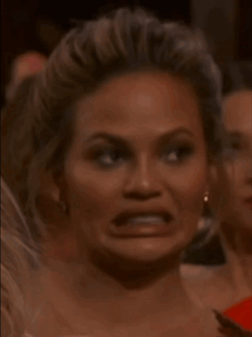 Chrissy Teigen in an audience grimacing with clenched teeth, the famous cringe face
