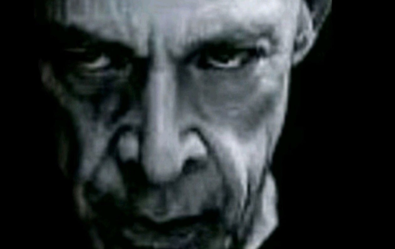 Intense elderly man looming out of darkness with a cold, menacing downward stare