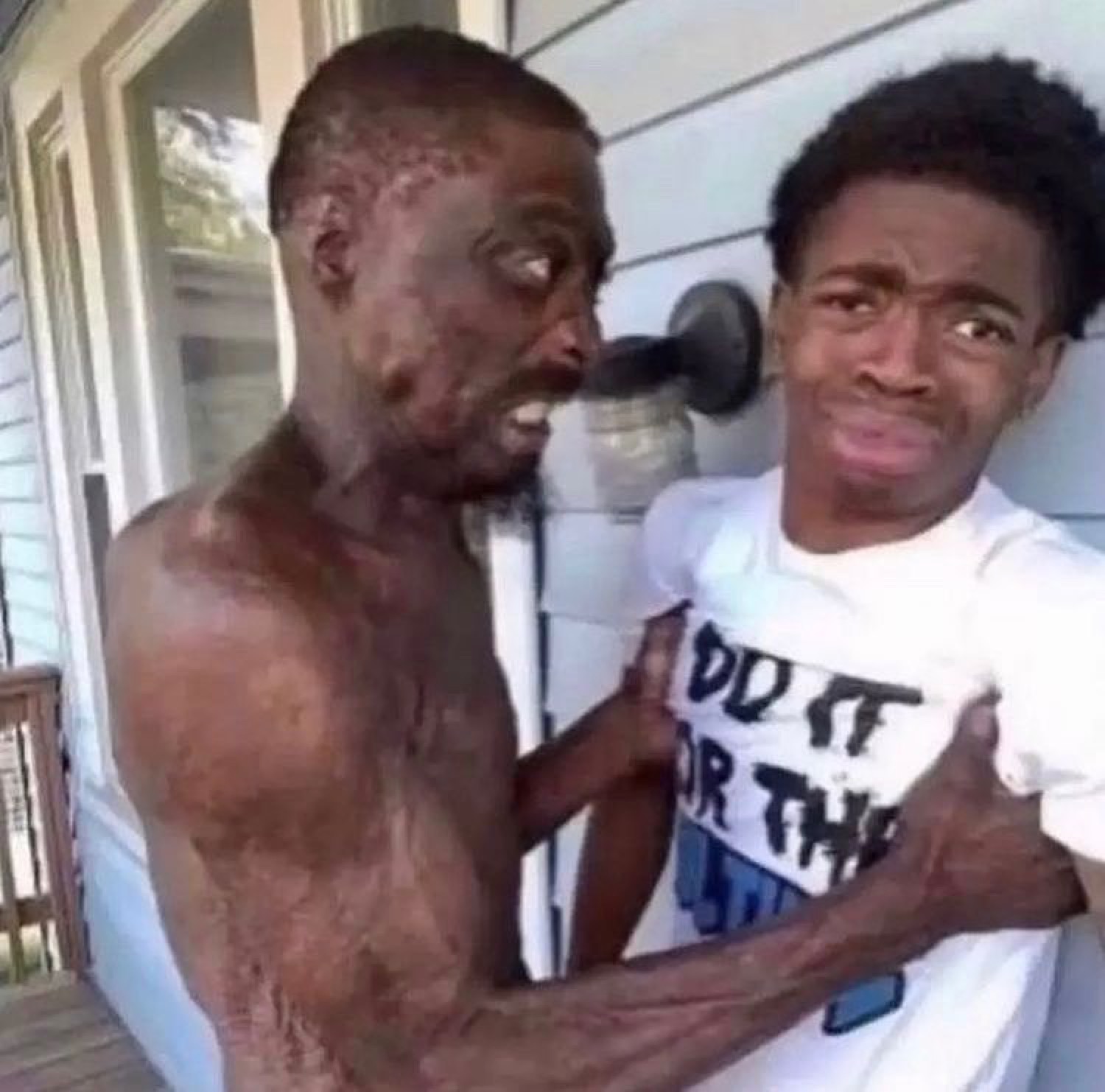 Gaunt man gripping a nervous kid in a 'DO IT FOR THE' shirt on a porch