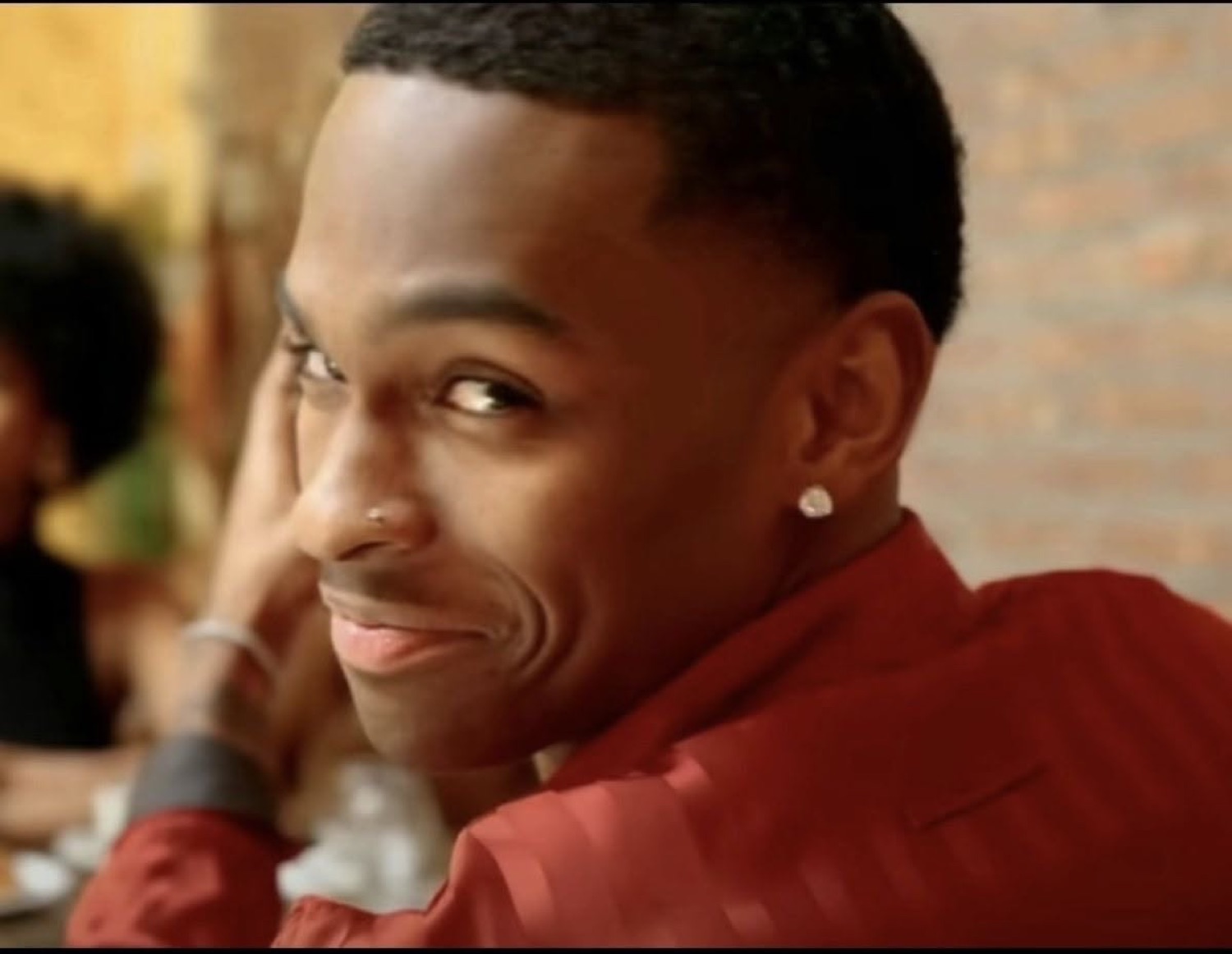 Guy in a red shirt resting his chin on his hand with a flirty little smirk