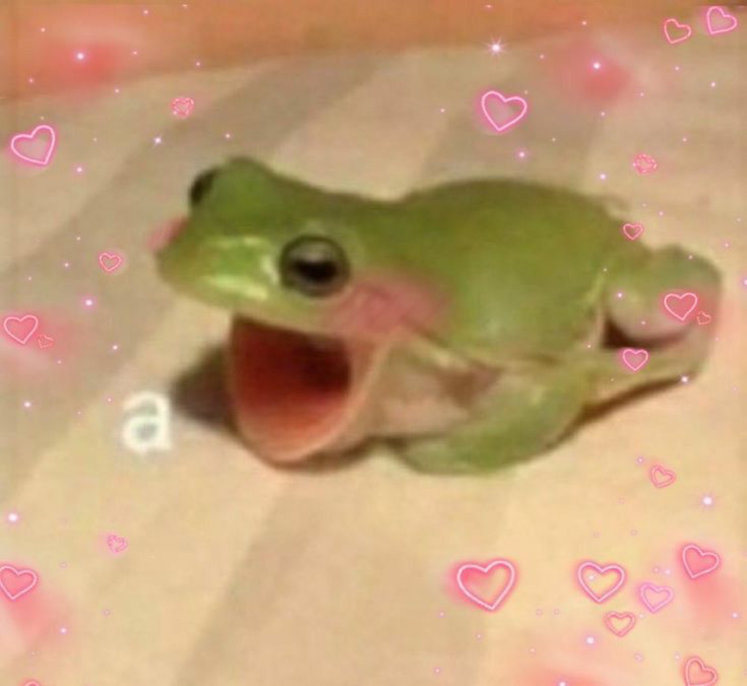 Happy green frog with wide open mouth surrounded by pink heart stickers and sparkles