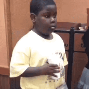 Boy in a yellow shirt holding a cup, glancing sideways with an awkward look