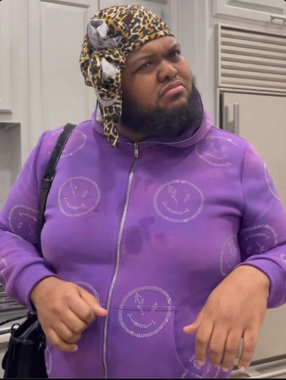 Man in a purple hoodie and head wrap with a confused shrug