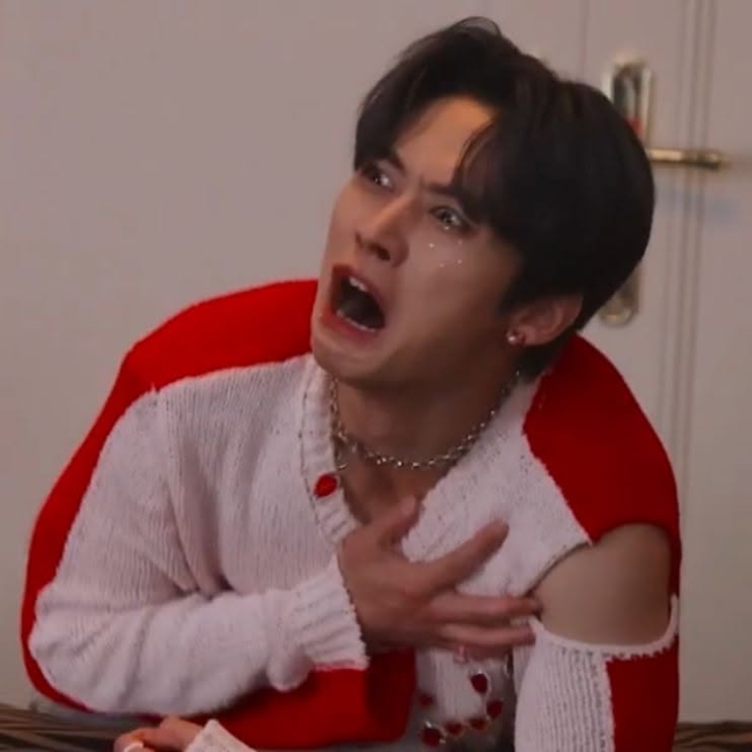Young man in white-and-red sweater crying and gasping with hand on chest