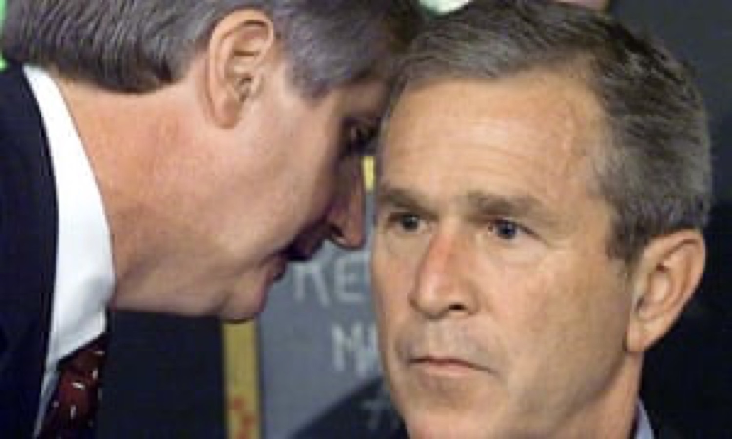 George W. Bush frozen with a blank stare as an aide whispers in his ear
