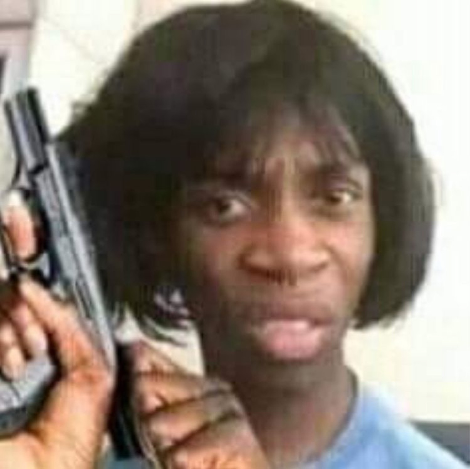 Person holding a handgun up beside their head with a flat, deadpan stare