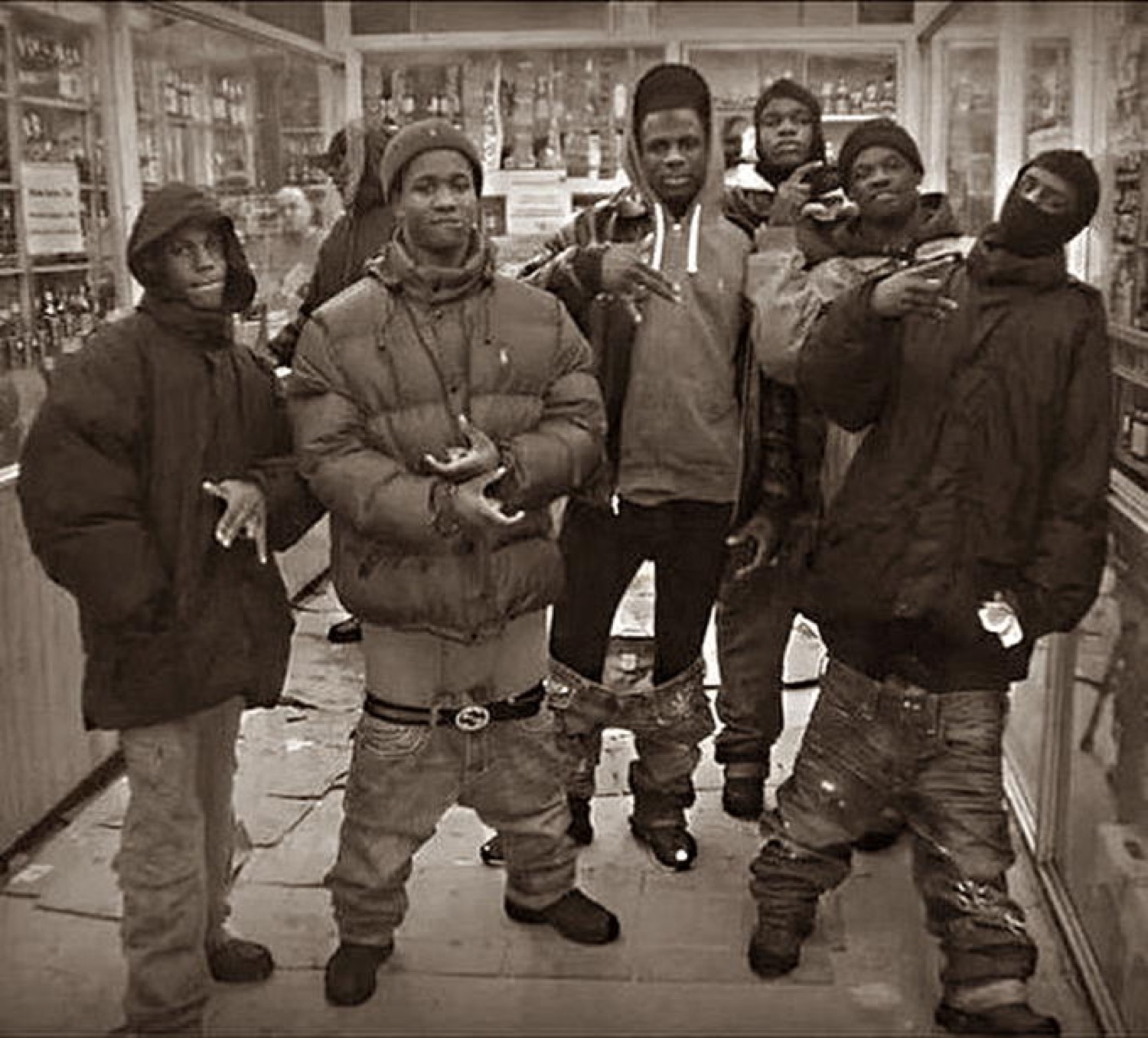 A group of young men in winter coats posing and throwing hand signs in a corner shop