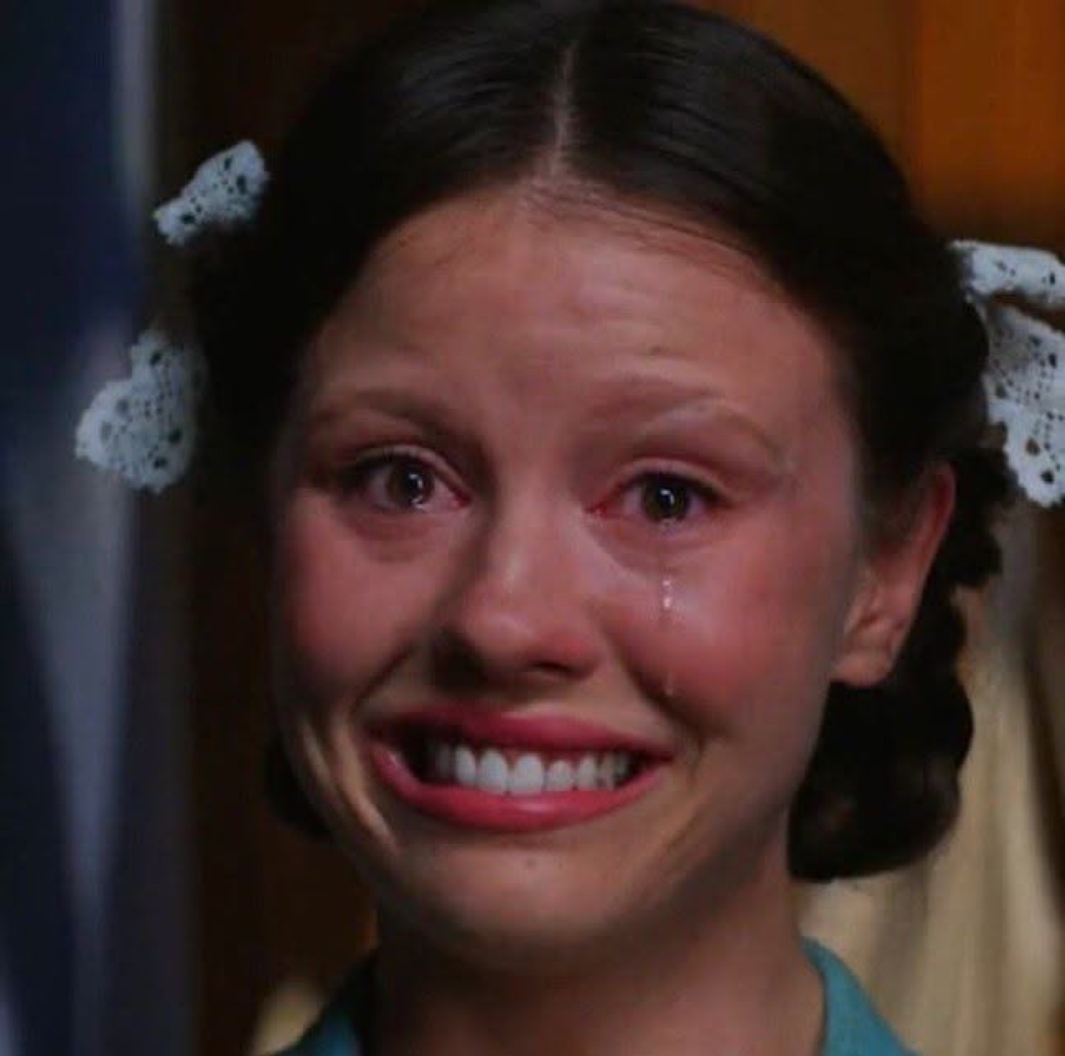 Young girl with pigtails and hair bows crying while forcing a smile through the tears