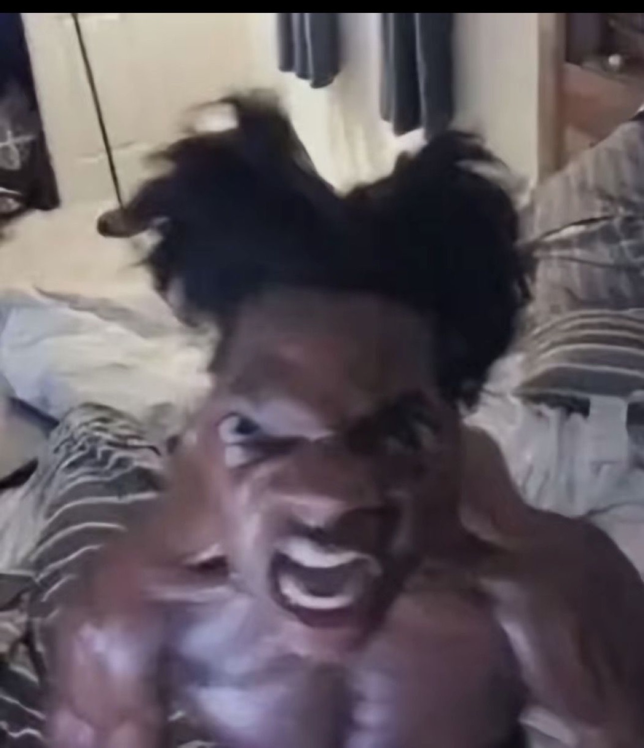 Shirtless man screaming with his hair wild and hands gripping his head