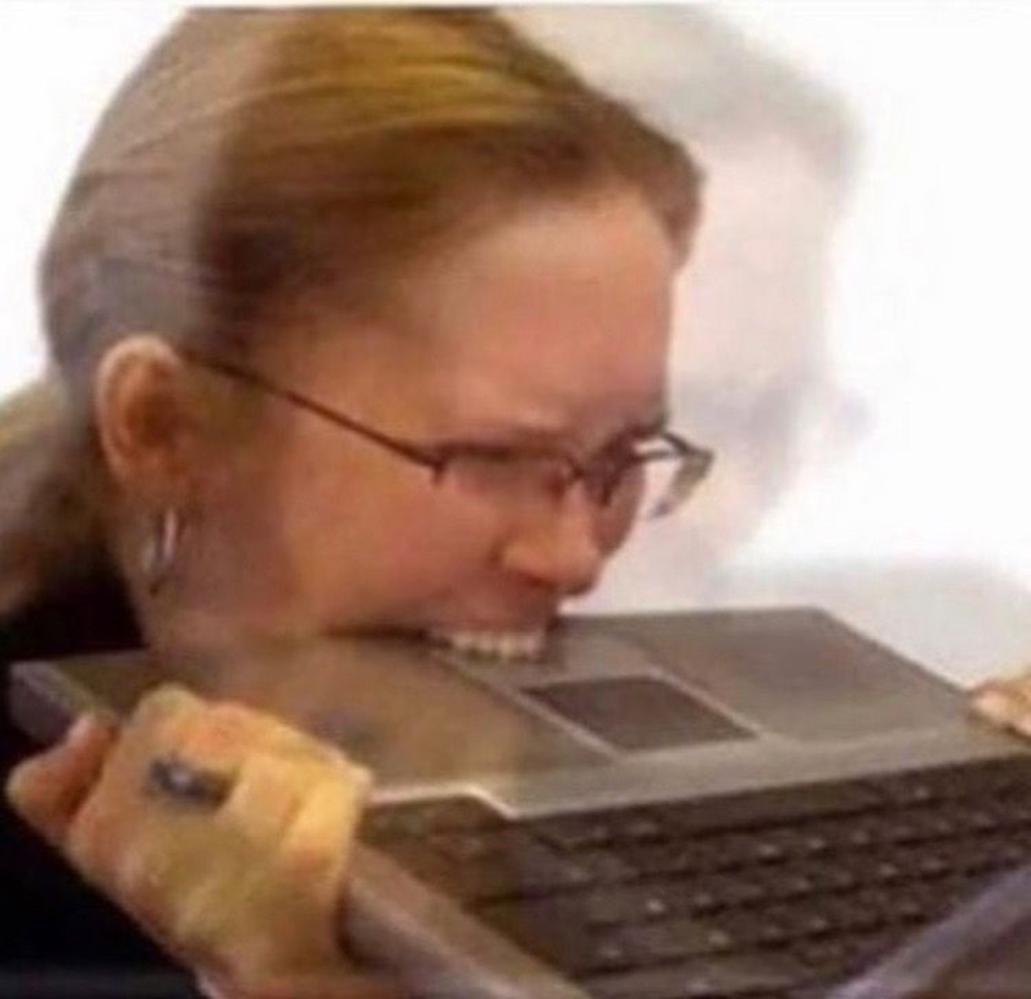 Woman in glasses biting down on a laptop in pure frustration as it smokes