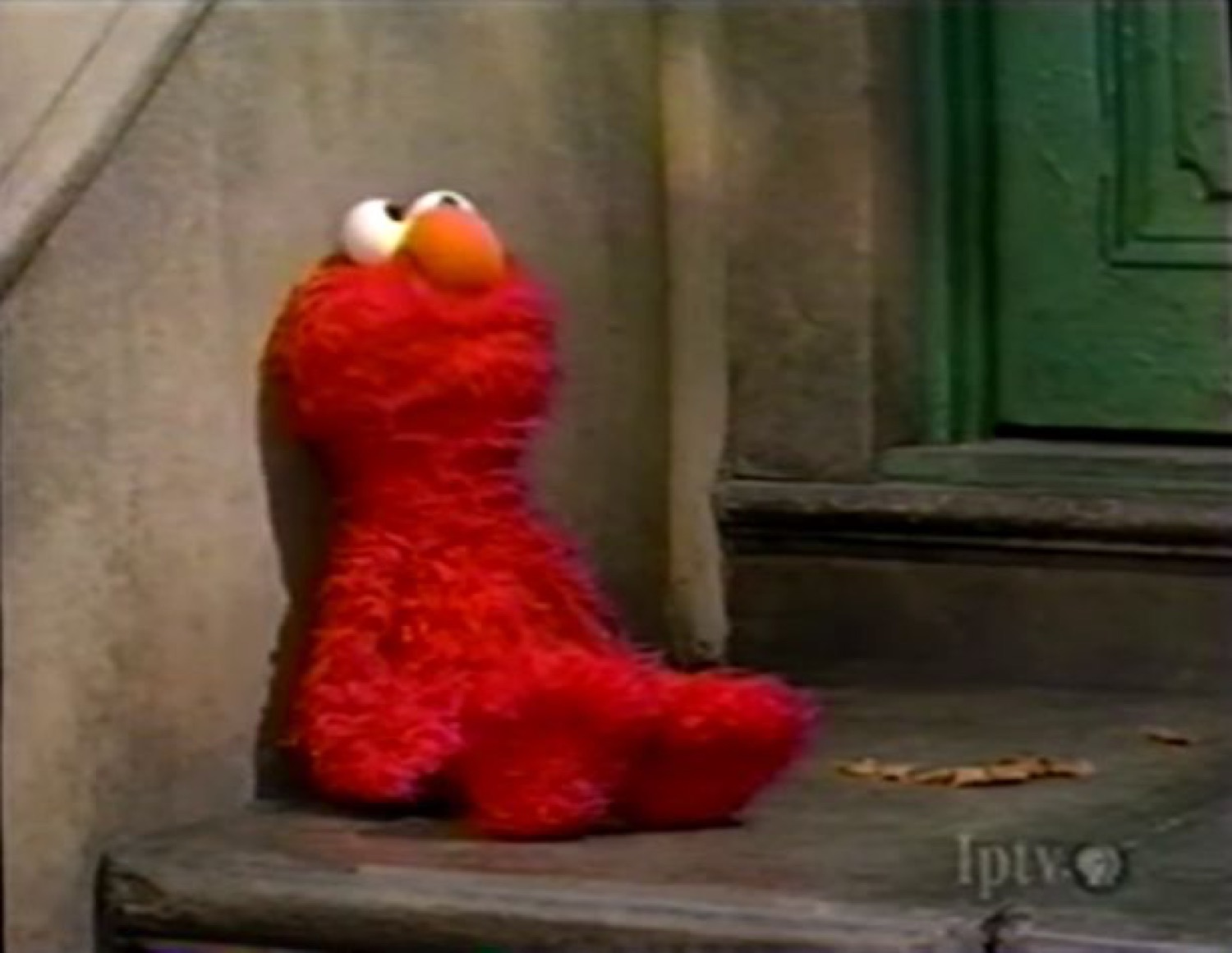 Elmo slumped alone on a stone stoop looking dejected