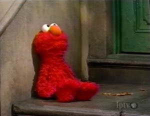 Elmo slumped alone on a stone stoop looking dejected