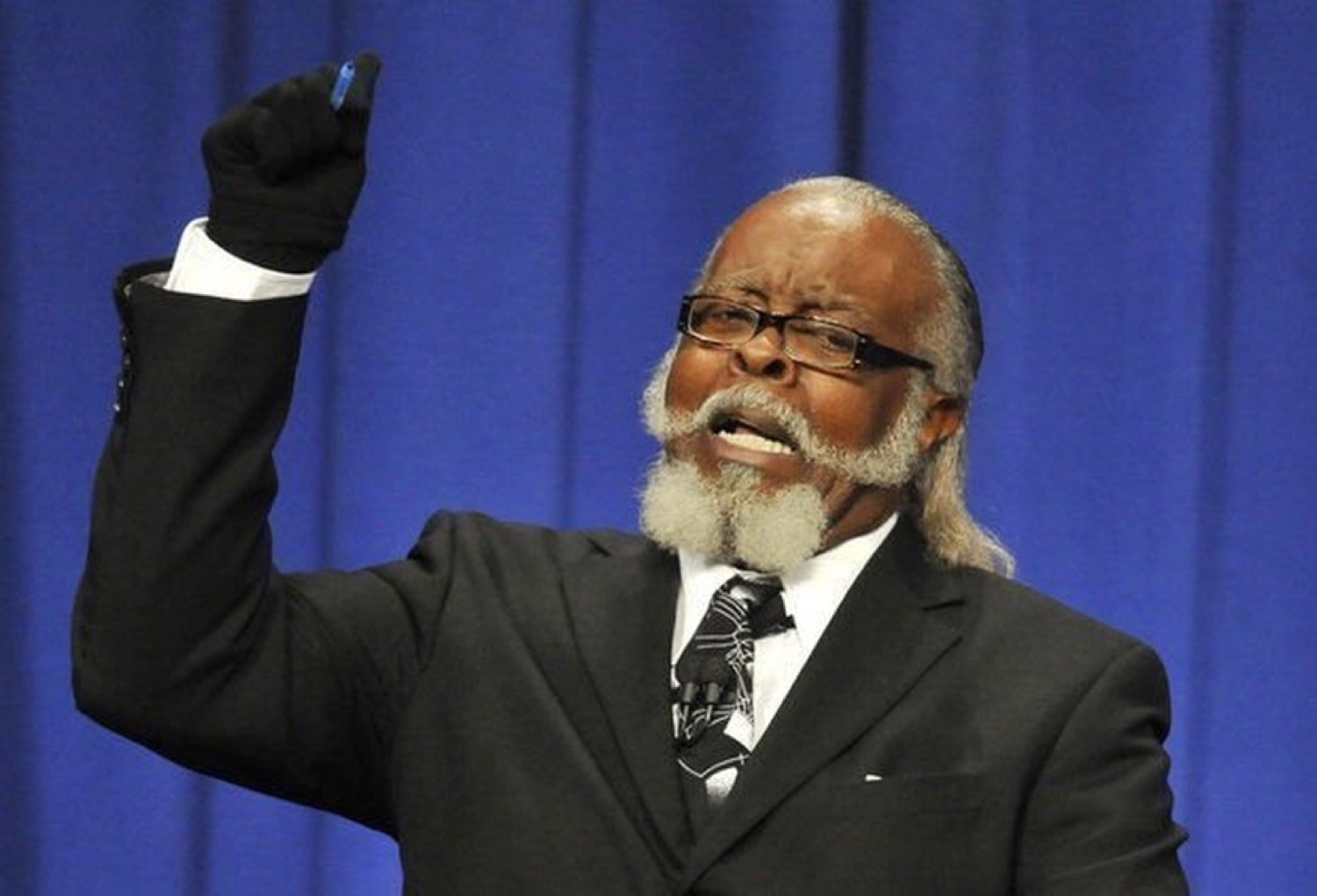 Older man in a suit and glove pointing intensely at something off-camera with full conviction