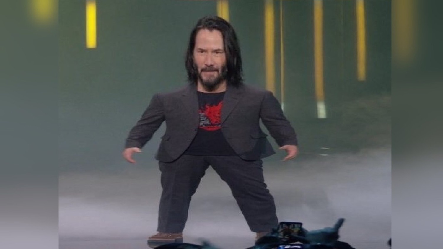 A shrunken-body Keanu Reeves standing awkwardly on stage in a suit and t-shirt