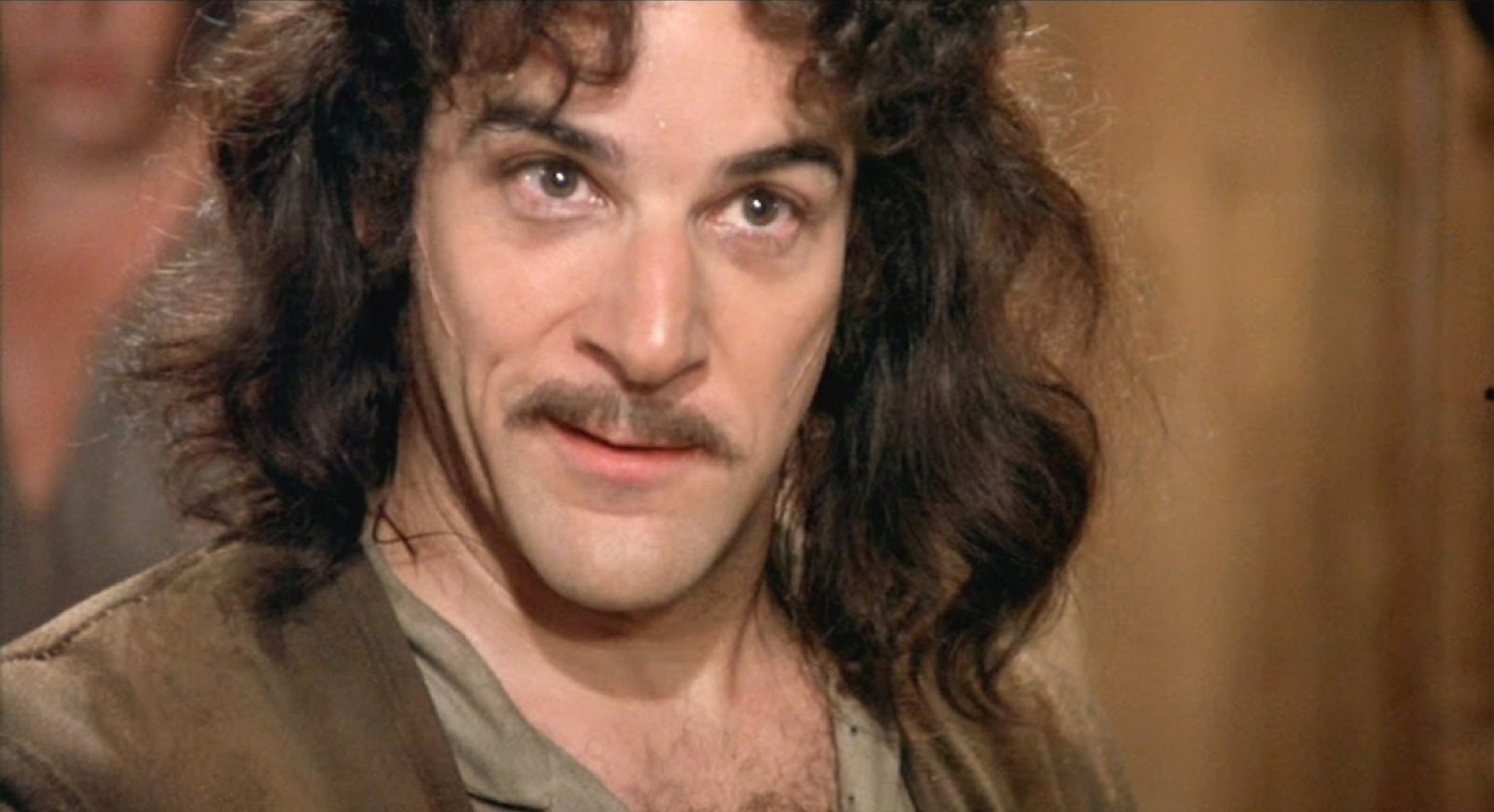 Long-haired mustached man tilting his head with a sly, knowing look