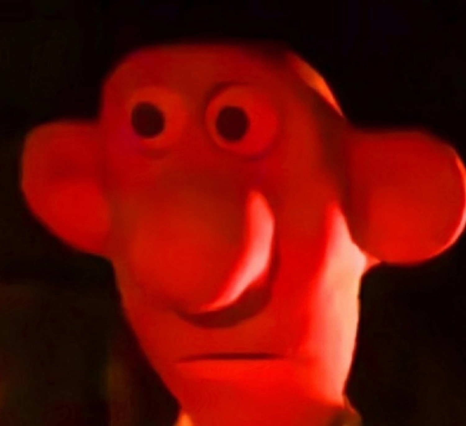 Red-lit claymation puppet grinning with a wide, unsettling stare