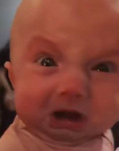 Newborn baby with wide startled eyes and a furrowed brow staring at the camera
