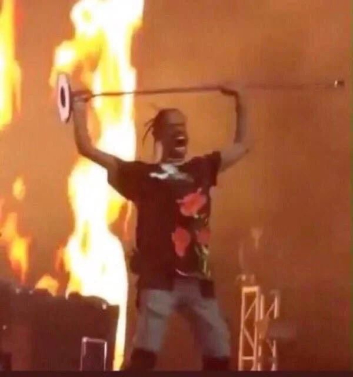 Rapper on stage screaming with arms raised as flames shoot up behind him