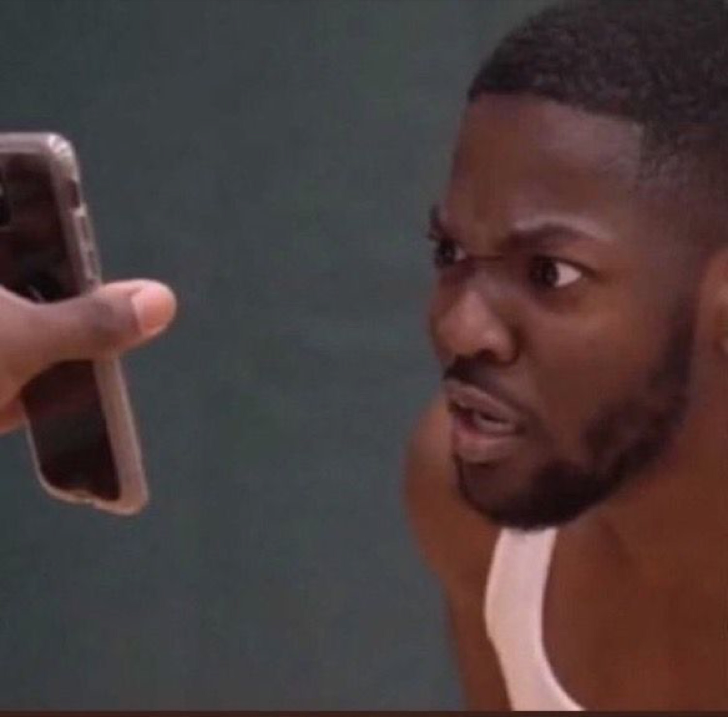 Man staring down a phone being held up at him, looking deeply skeptical