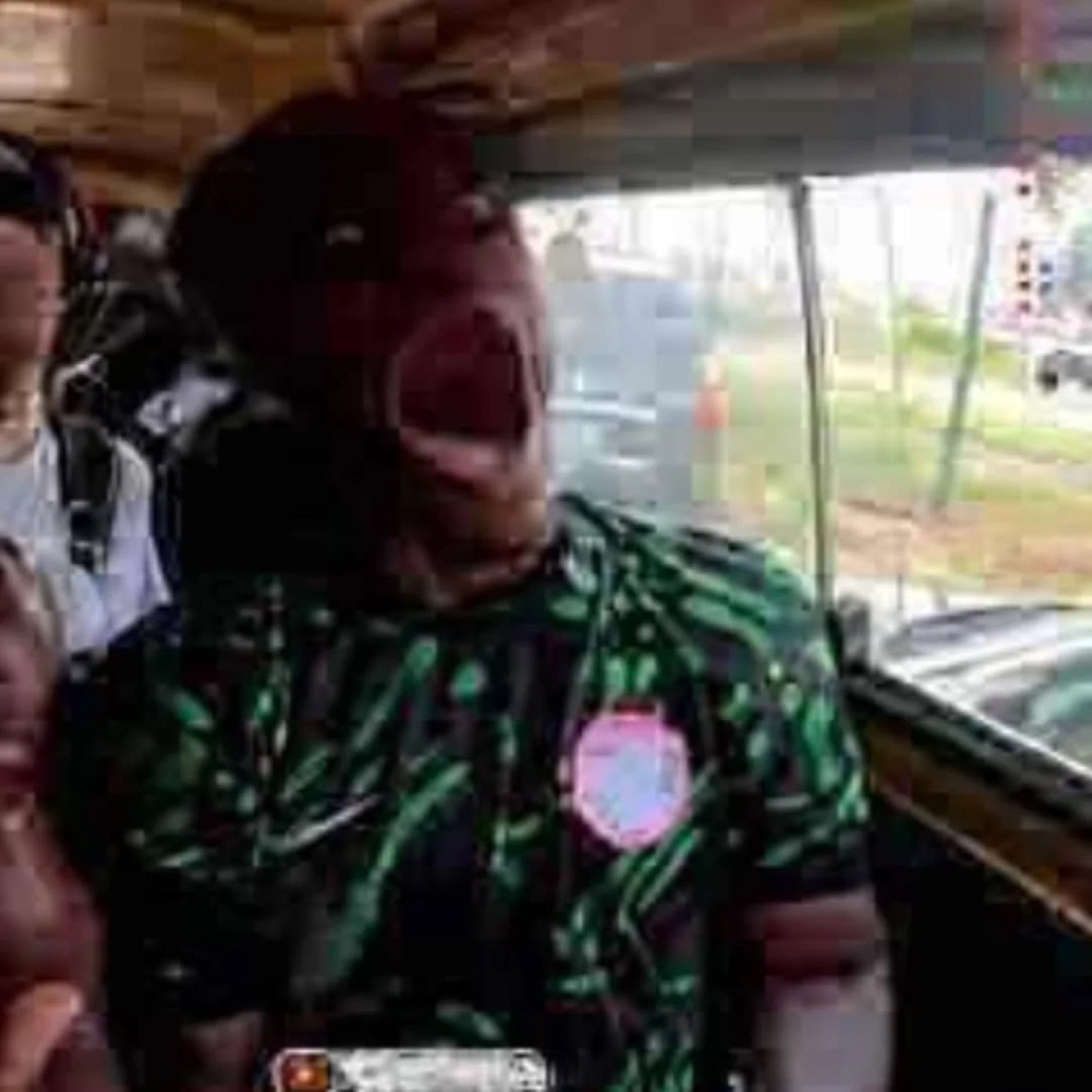 Person in a green print shirt screaming with mouth wide open inside a crowded vehicle
