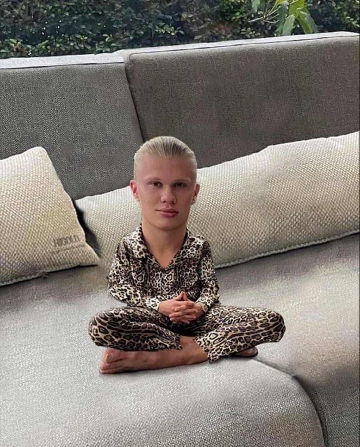 Blond man in leopard-print pajamas sitting cross-legged on a couch with a blank stare