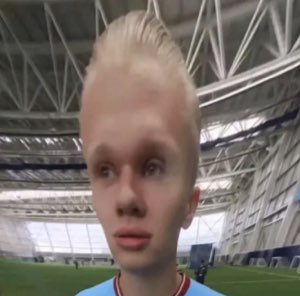 Blond footballer with a face-warp filter making him look unsettlingly baby-faced on a stadium pitch