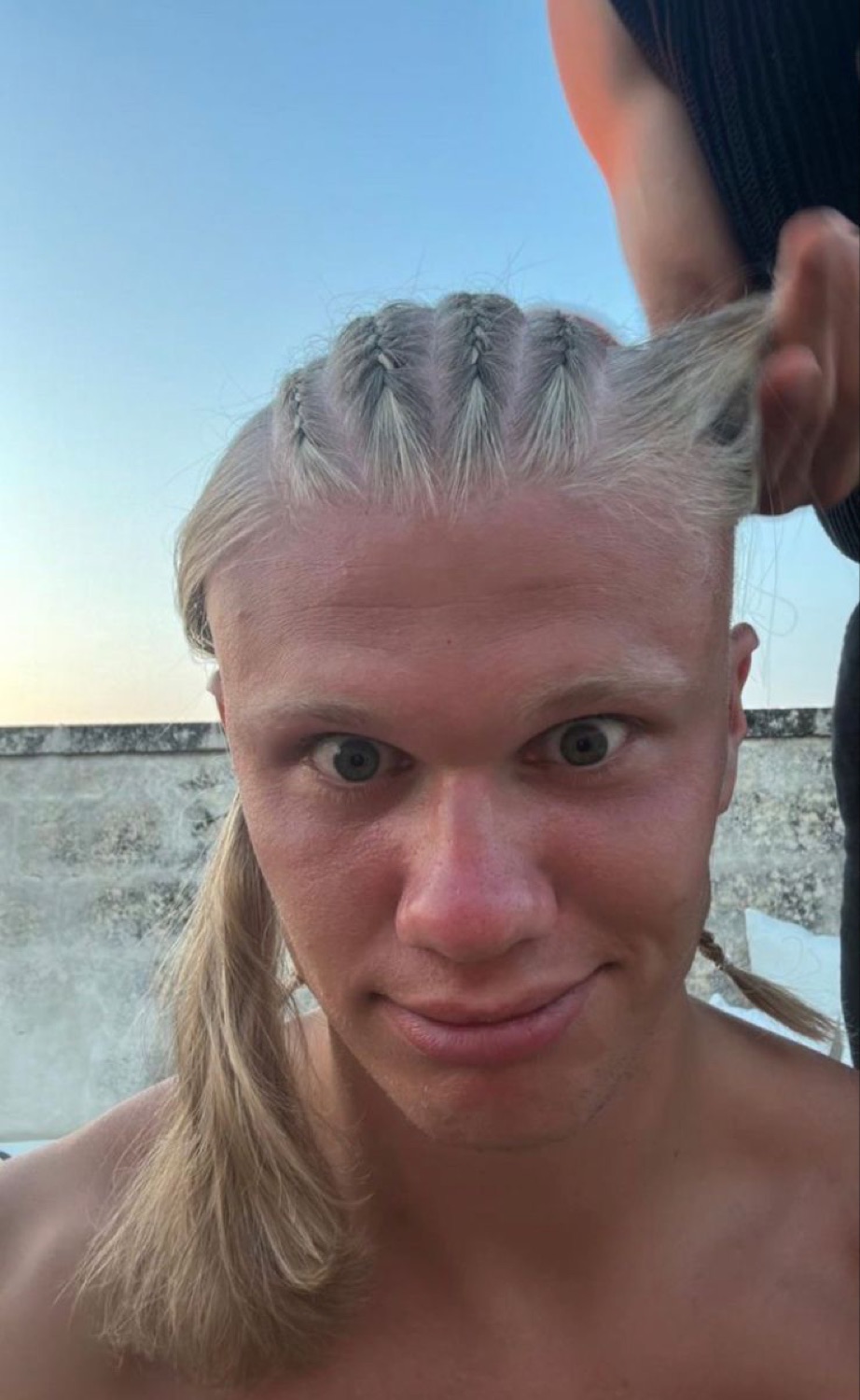 Erling Haaland getting his hair braided, staring at the camera with a goofy tight-lipped look