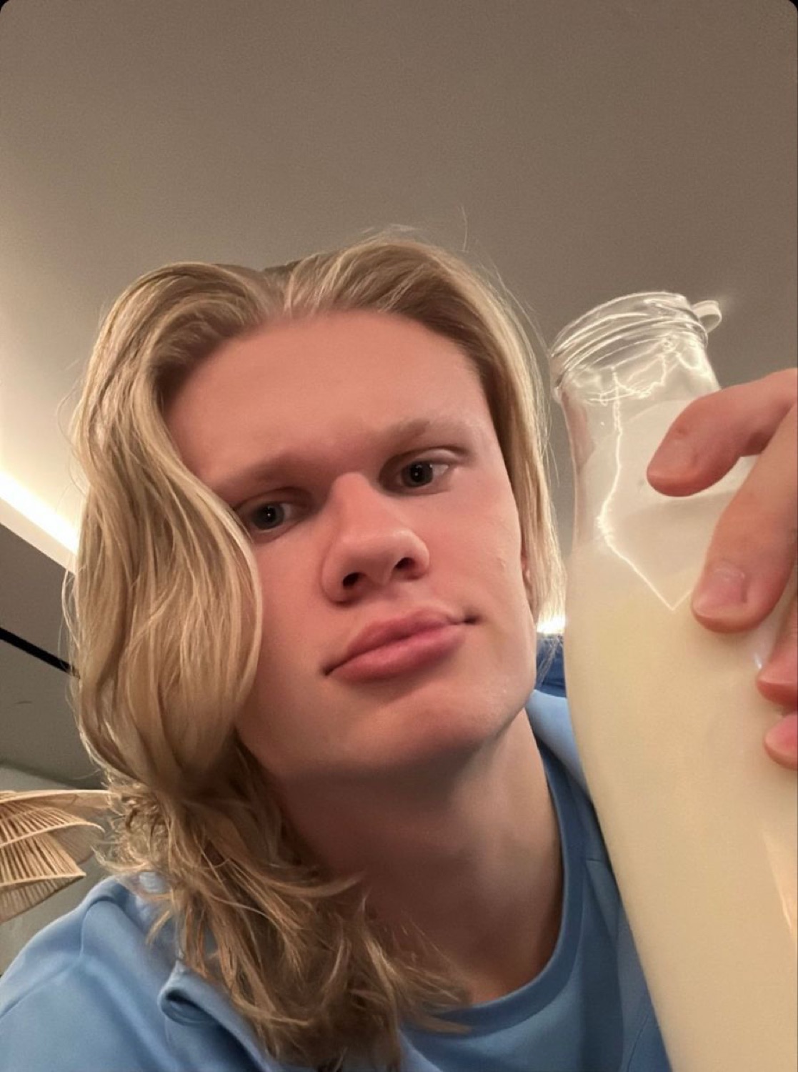 Long-haired young man holding a bottle of milk with a flat, deadpan selfie face