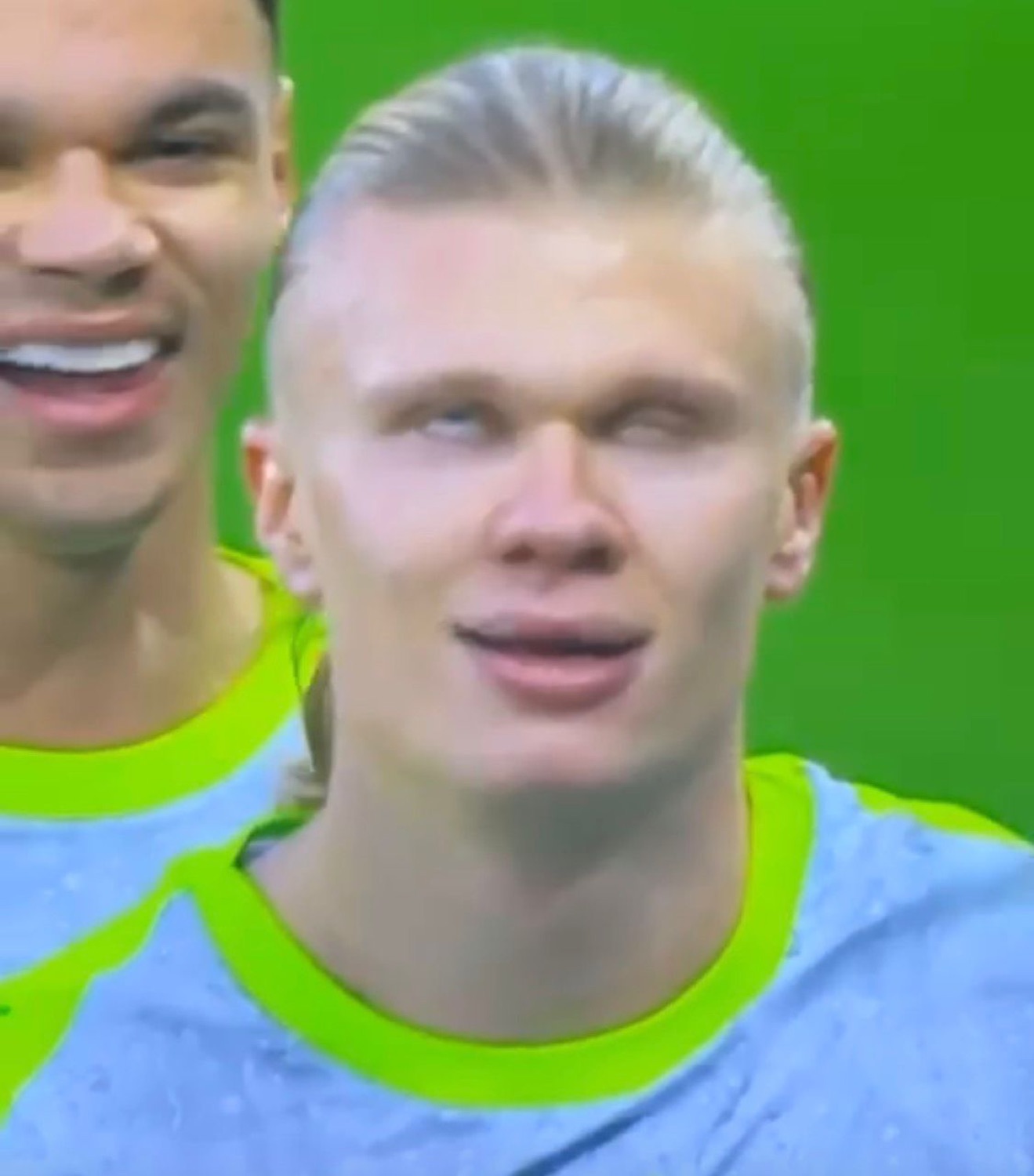 Blond footballer in a light blue kit smirking and glancing sideways on the pitch