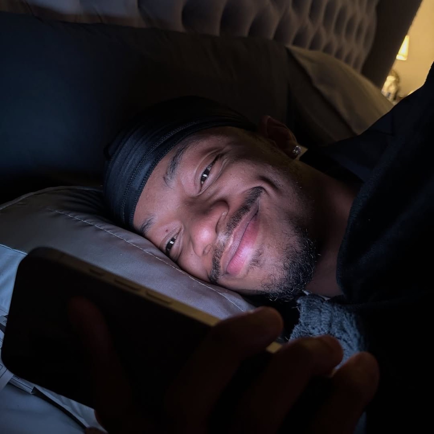 Man lying in bed at night on his phone with a soft, smug smirk