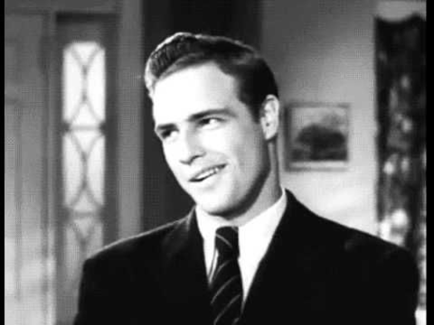 Vintage black-and-white shot of a suited young man with a sly, charming smirk